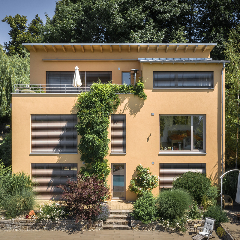 Neues Einfamilienhaus mit gelber Fassade, begrüntem Garten und großer Terrasse.