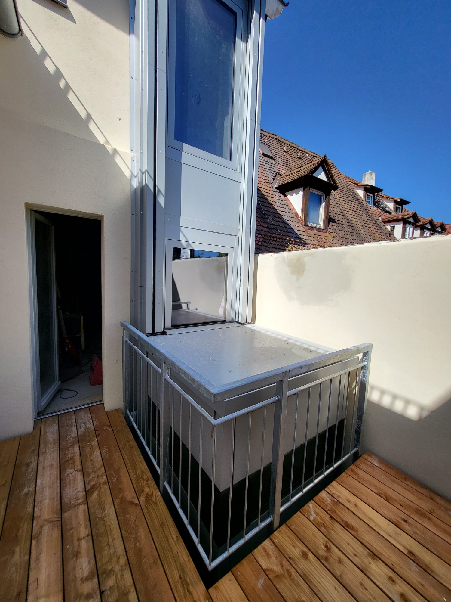 Ein schmaler Balkon mit Metallgeländer, Holzboden und einer offenen Tür.